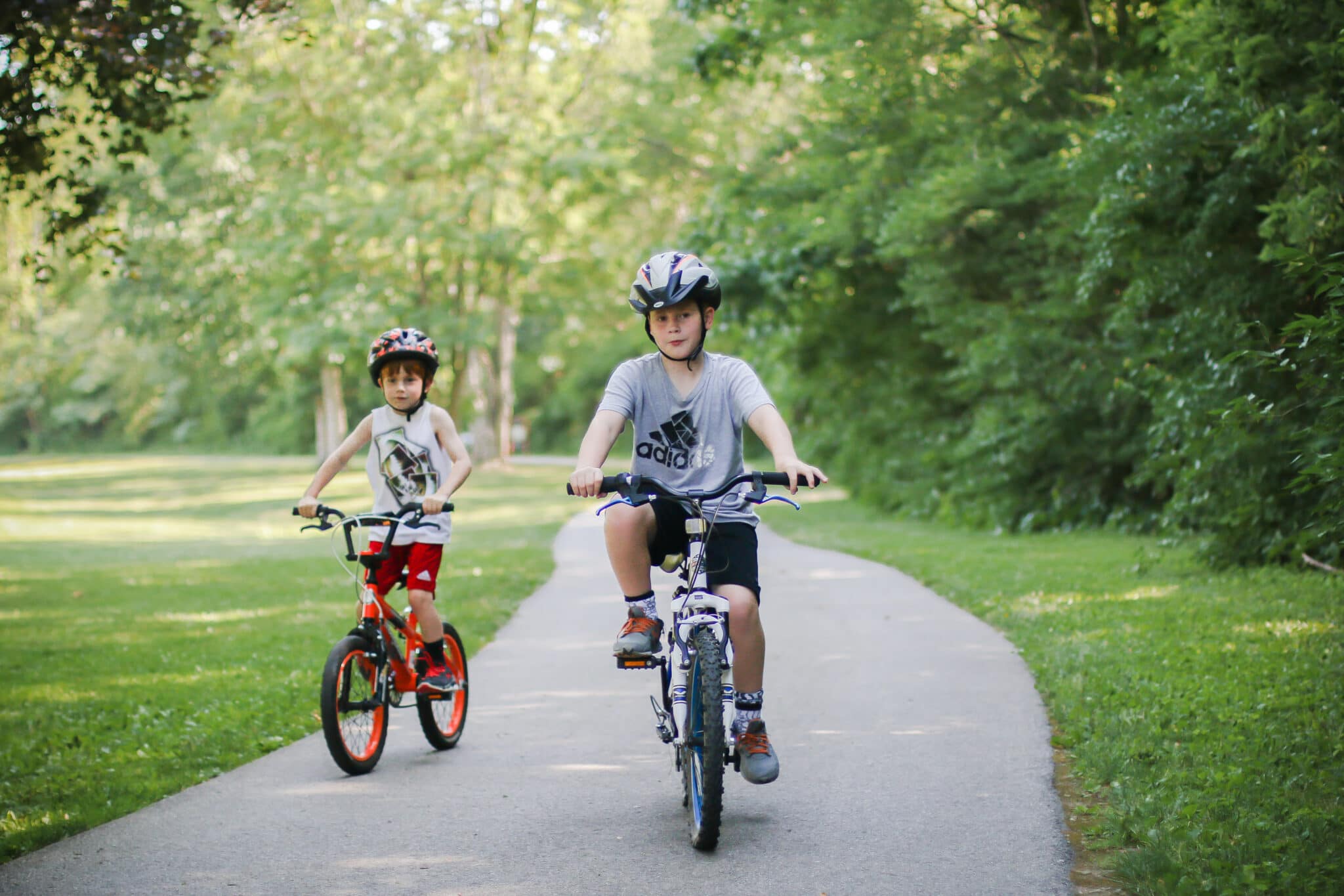 Two young wearing helmets riding bicycles on paved path at Mingo Park